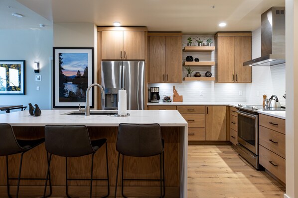 Une cuisine moderne avec des meubles en bois, des appareils en acier inoxydable et un coin bar équipé de tabourets.