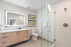 A modern bathroom with a glass shower enclosure, a white toilet, and a vanity with a large mirror.
