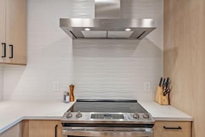 A kitchen with a stainless steel range hood, a built-in oven, and a countertop with a pepper grinder and knives. - Scarlet Tanager | Includes Two 1-Day Lift Tickets (Tamarack)