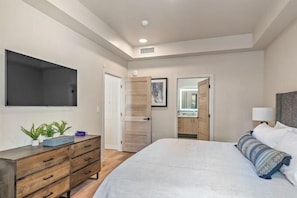 A bedroom with a bed, a dresser, a TV, and a door leading to a bathroom. - Scarlet Tanager | Includes Two 1-Day Lift Tickets (Tamarack)