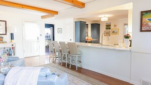 Una cocina moderna con barra, vigas de madera, armarios blancos y una isla grande con taburetes de bar.