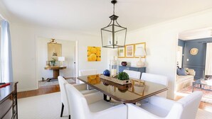 Un comedor con mesa de vidrio, sillas blancas y lámpara colgante.