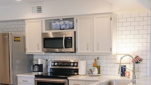 Una cocina moderna con armarios blancos, un refrigerador de acero inoxidable, un microondas, un horno y un lavamanos.