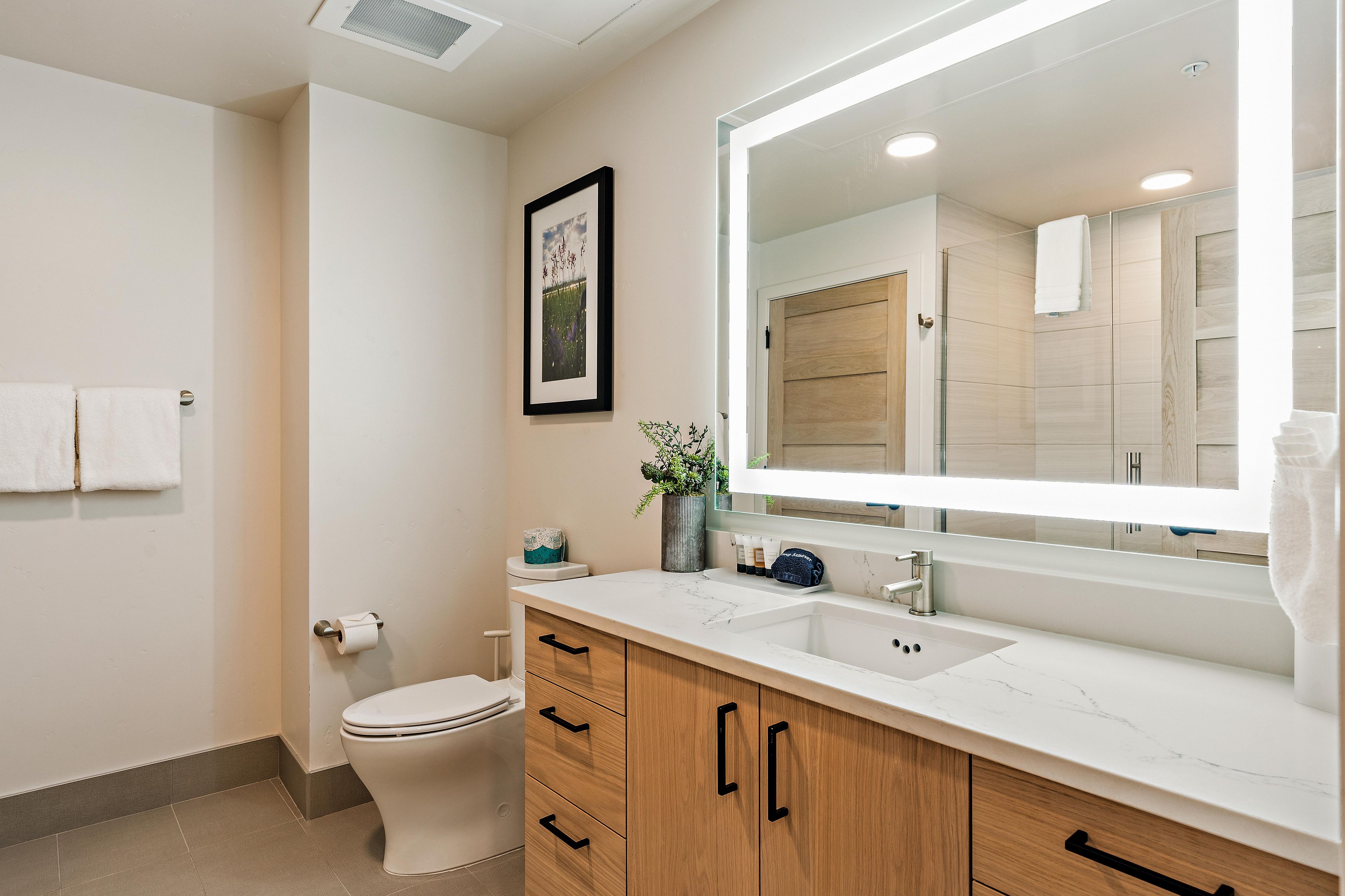 A modern bathroom with a toilet, sink, vanity, and a large mirror.