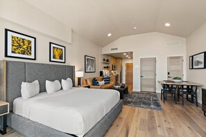 A hotel room with a large bed, a desk, a chair, and a dining table. There are framed pictures on the wall and a door leading to the bathroom. - Panoramic Views| Exclusive Tamarack Perks (Tamarack)