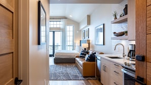 A modern hotel room with a bed, a sofa, a kitchen area with a sink and stove, and a balcony with a view. - Panoramic Views| Exclusive Tamarack Perks (Tamarack)