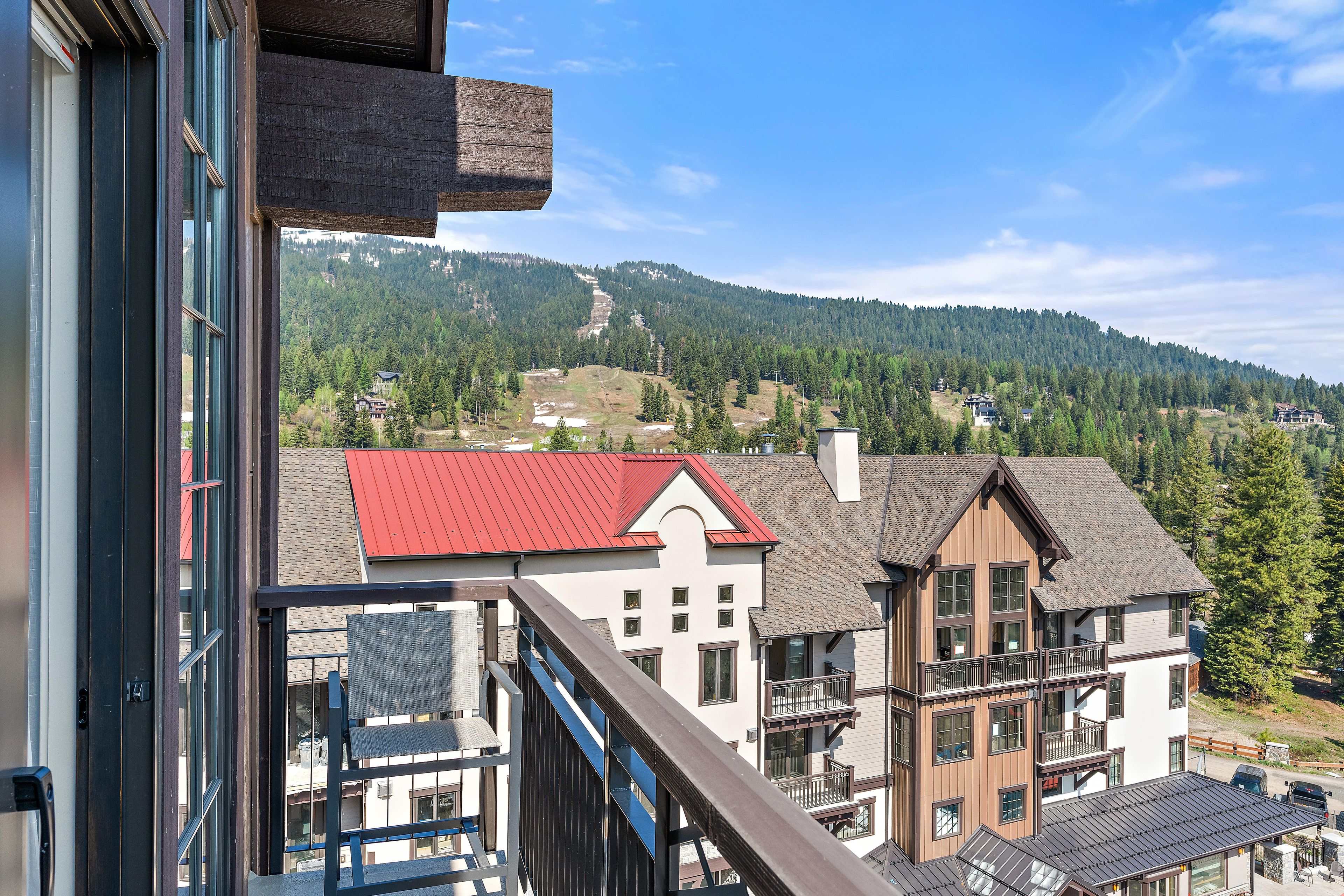 A view from a balcony with a mountain backdrop, featuring a building with a red roof and a white facade.