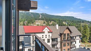 A view from a balcony with a mountain backdrop, featuring a building with a red roof and a white facade.