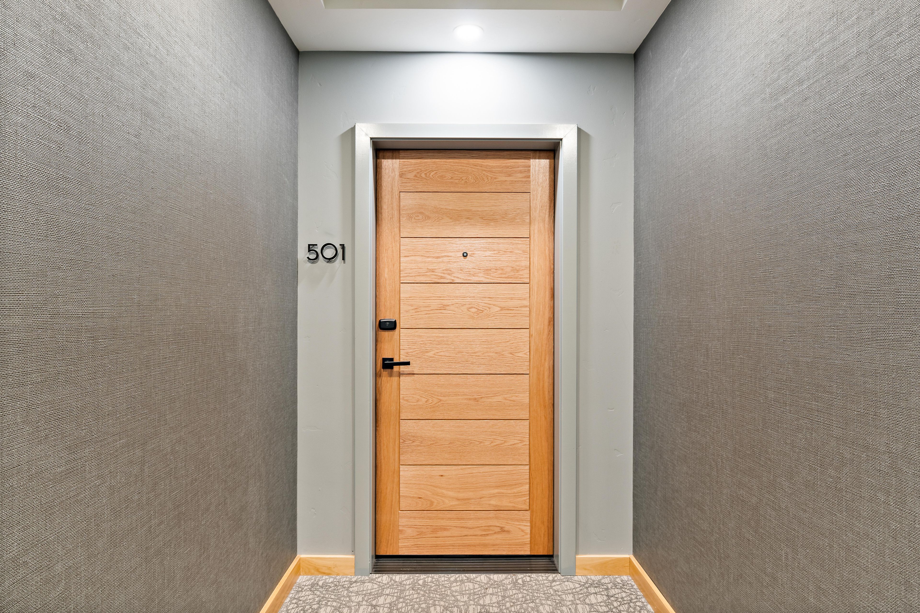 A hallway with a wooden door marked with the number 501, a textured wall, and a patterned carpet.