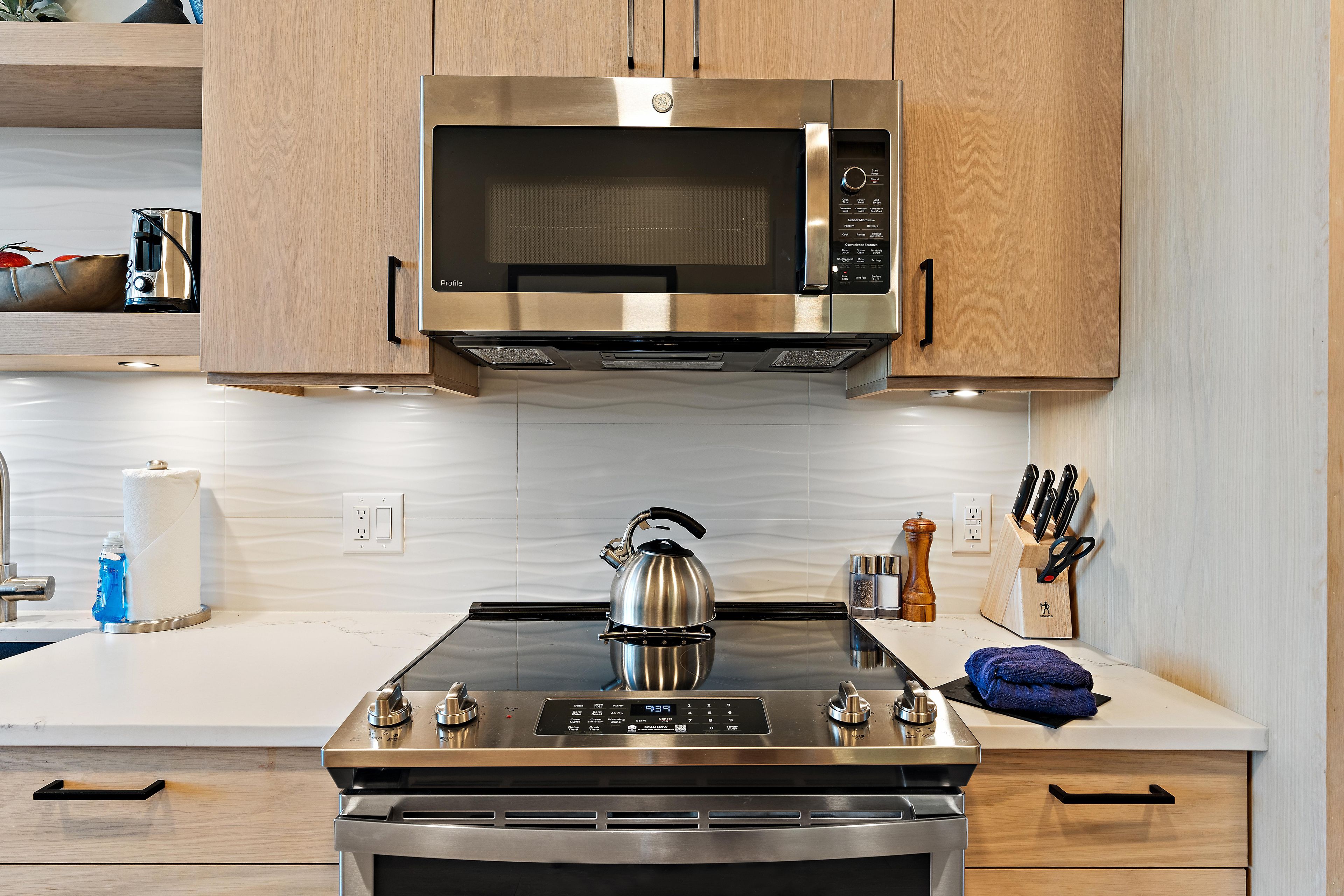 Una cocina con estufa de acero inoxidable, hervidor y microondas encima.