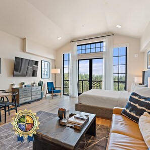 A spacious room with a bed, a sofa, a TV mounted on the wall, and a large window offering a view of the outdoors. - Panoramic Views| Exclusive Tamarack Perks (Tamarack)