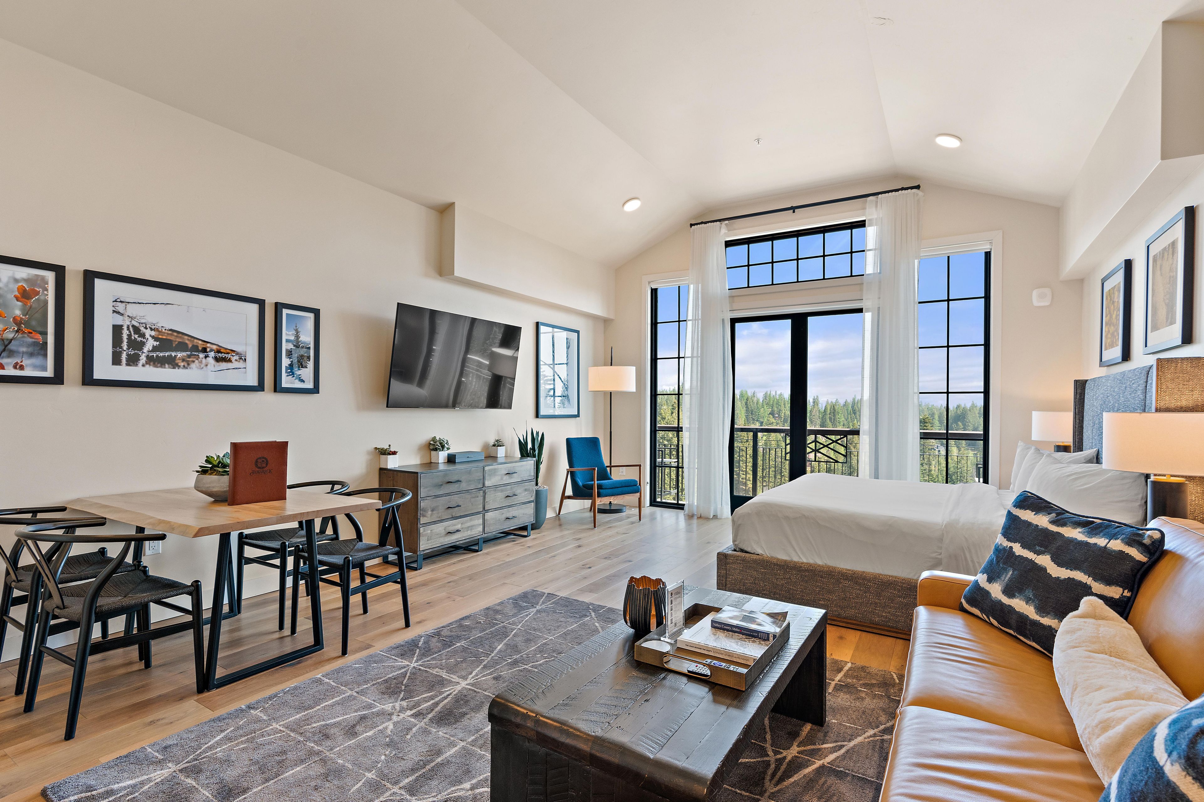 A spacious living area with a large bed, a dining table, and a TV mounted on the wall.
