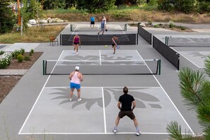 Un court de tennis en plein air où plusieurs personnes peuvent jouer, avec des bancs et une zone paysagée qui l’entoure.