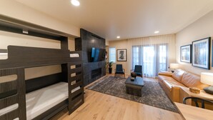 Une chambre d’hôtel moderne équipée de lits superposés, d’un téléviseur à écran plat, d’un canapé, d’une table basse et d’une table à manger.