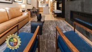 Un salon moderne avec un canapé, une table basse et une cheminée. On aperçoit une cuisine à l’arrière-plan, avec un coin repas.