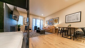 Ein modernes Hotelzimmer mit Bett, einer Sitzecke mit Sofa und Sesseln, einem Esstisch und Kunstwerken an den Wänden.