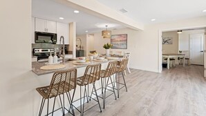 Uma cozinha moderna com uma ilha central, banquetas e uma área de jantar com mesa e cadeiras.