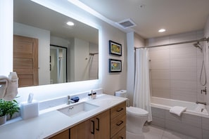 Une salle de bain moderne avec un grand miroir, un lavabo, des toilettes et une baignoire.