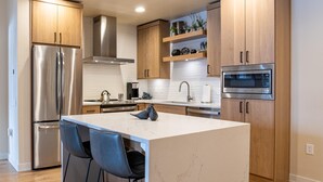 Een moderne keuken met een centraal eiland, roestvrijstalen apparatuur, houten kastjes en een marmeren aanrecht.