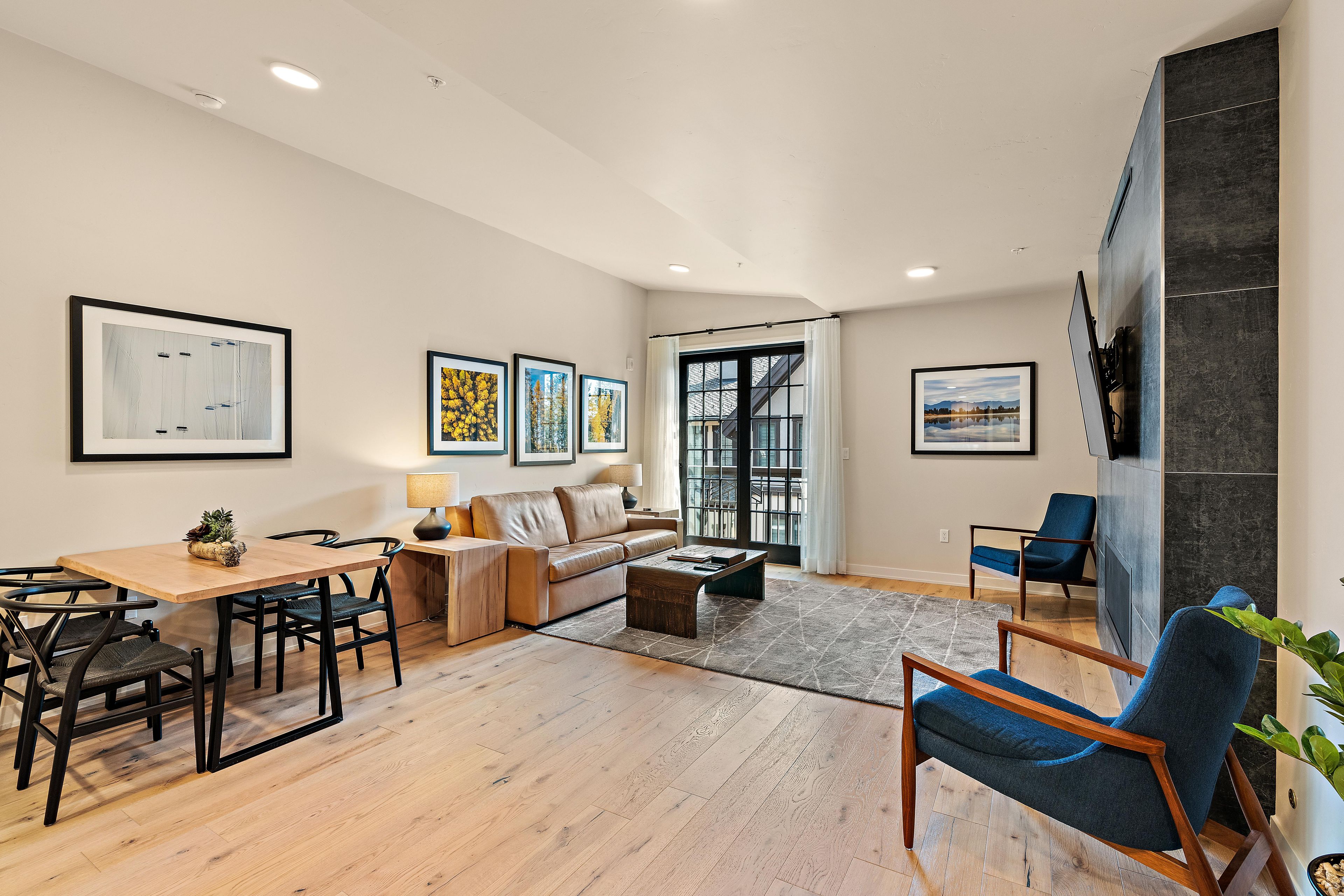 A modern living room with a dining area, a sofa, a coffee table, and a TV mounted on the wall.