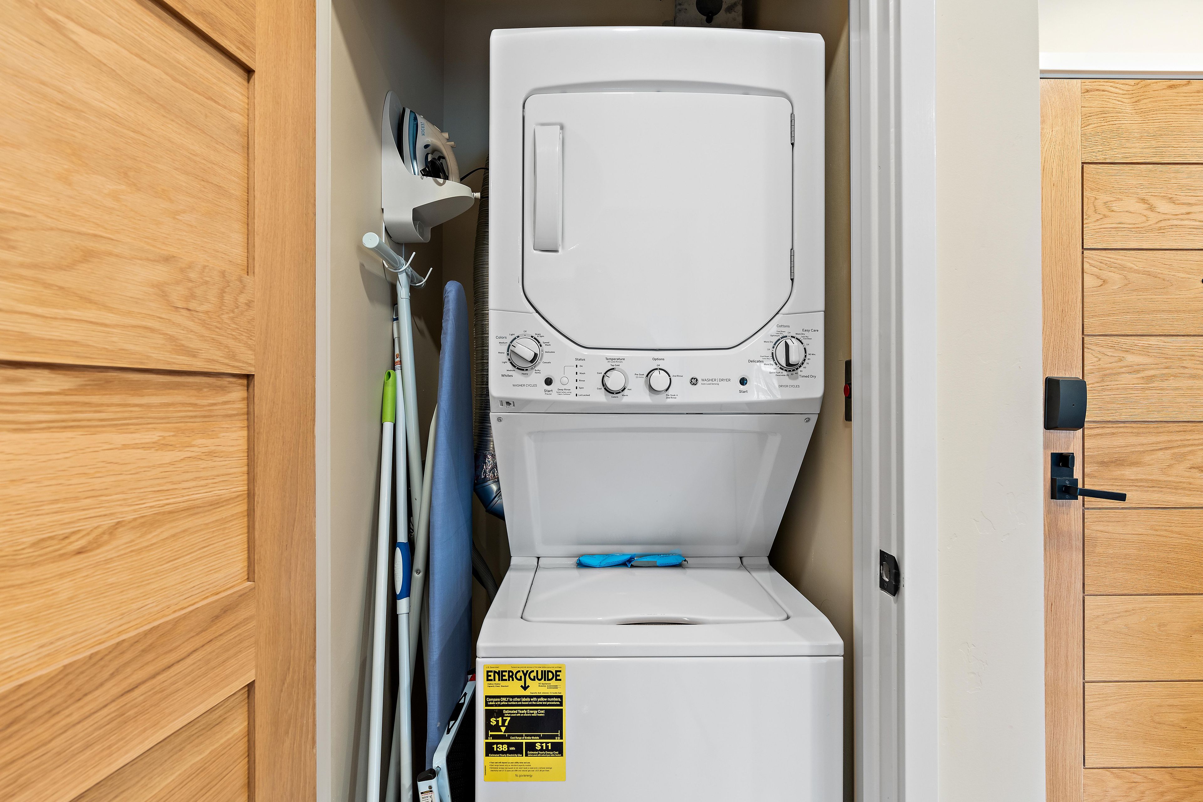 Un appareil compact combinant lave-linge et sèche-linge, doté d’un panneau de commande, d’une étiquette jaune indiquant les performances énergétiques et d’une serviette bleue suspendue à proximité.