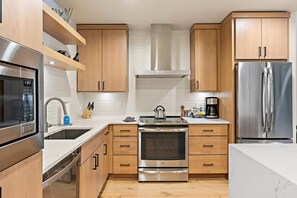 Una cocina moderna con electrodomésticos de acero inoxidable, armarios de madera y una encimera blanca.