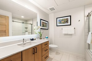 A modern bathroom with a large mirror, a shower, a toilet, and a sink with a vanity.