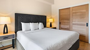 Habitación de hotel con una cama grande, dos mesitas de noche con lámparas, un armario de madera y una rejilla de ventilación en el techo.