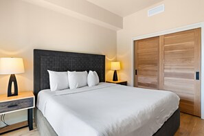 A hotel room with a large bed, two bedside tables with lamps, a wooden wardrobe, and a ceiling vent.