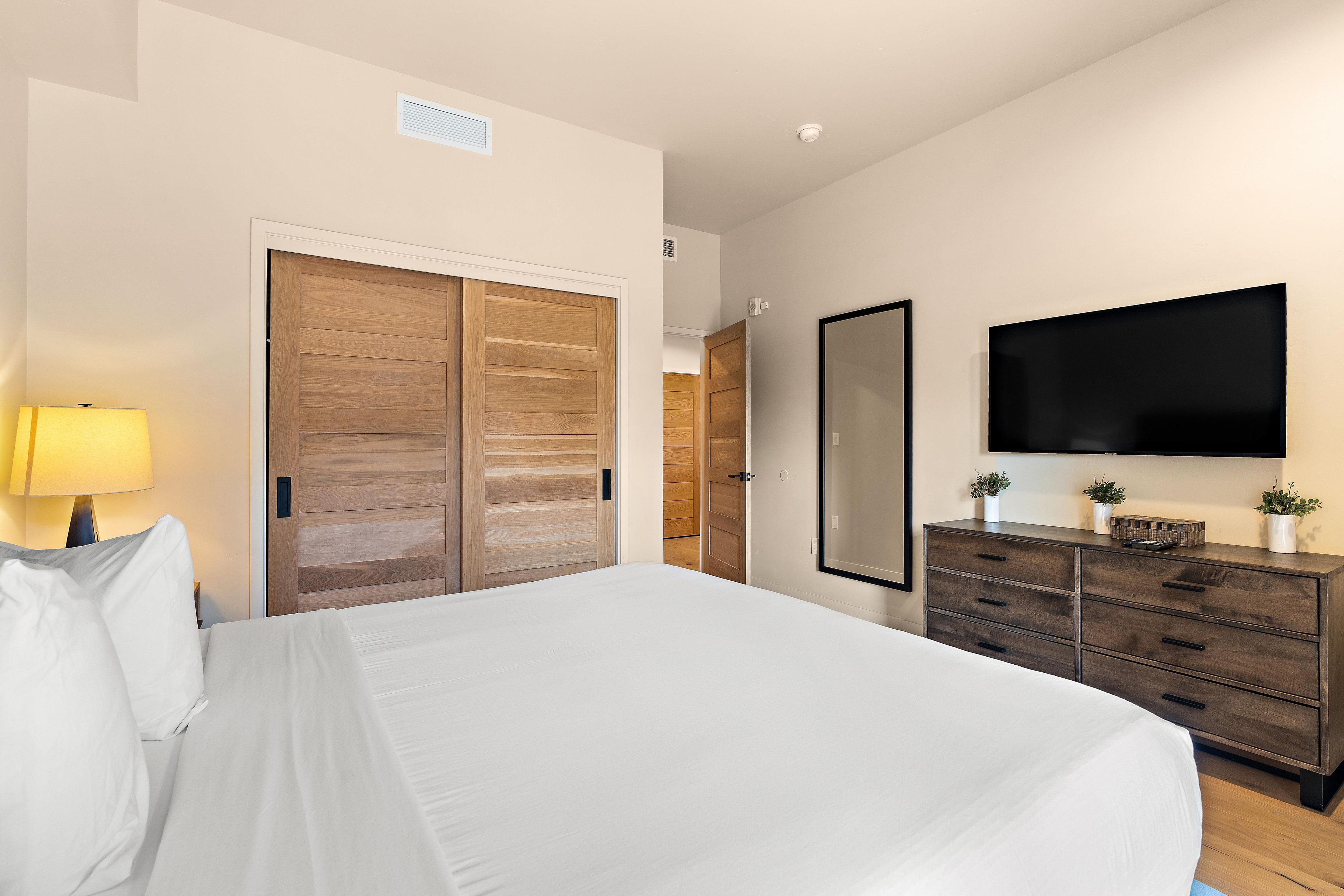 Ein Hotelzimmer mit einem großen Bett, einem Schminktisch, einem an der Wand befestigten Fernseher und einer Tür mit Holzpaneelen.