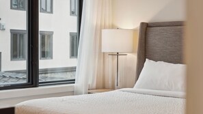 Une chambre d’hôtel avec un lit, une table de chevet, une lampe et une fenêtre avec des rideaux.