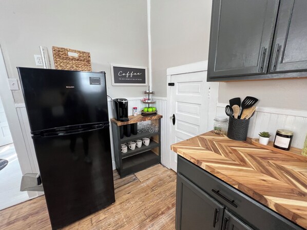 A compact kitchen with a black refrigerator, wooden countertops, and a white door. - The Cardinal Cottage: Charming 1930s Restored Farmhouse In the Heart of Webster (Webster)