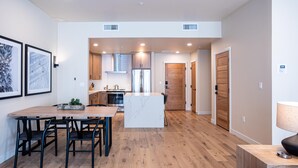 A modern kitchen with a central island, wooden flooring, and a dining area with a table and chairs. - Wind-Walker | Includes Two 1-Day Lift Tickets (Tamarack)
