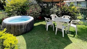 Area patio esterna con vasca idromassaggio, sedie di plastica bianca e un ombrellone grande.