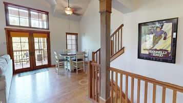 A spacious living area with a wooden floor, a dining table with chairs, a sofa, and a staircase with wooden railings.