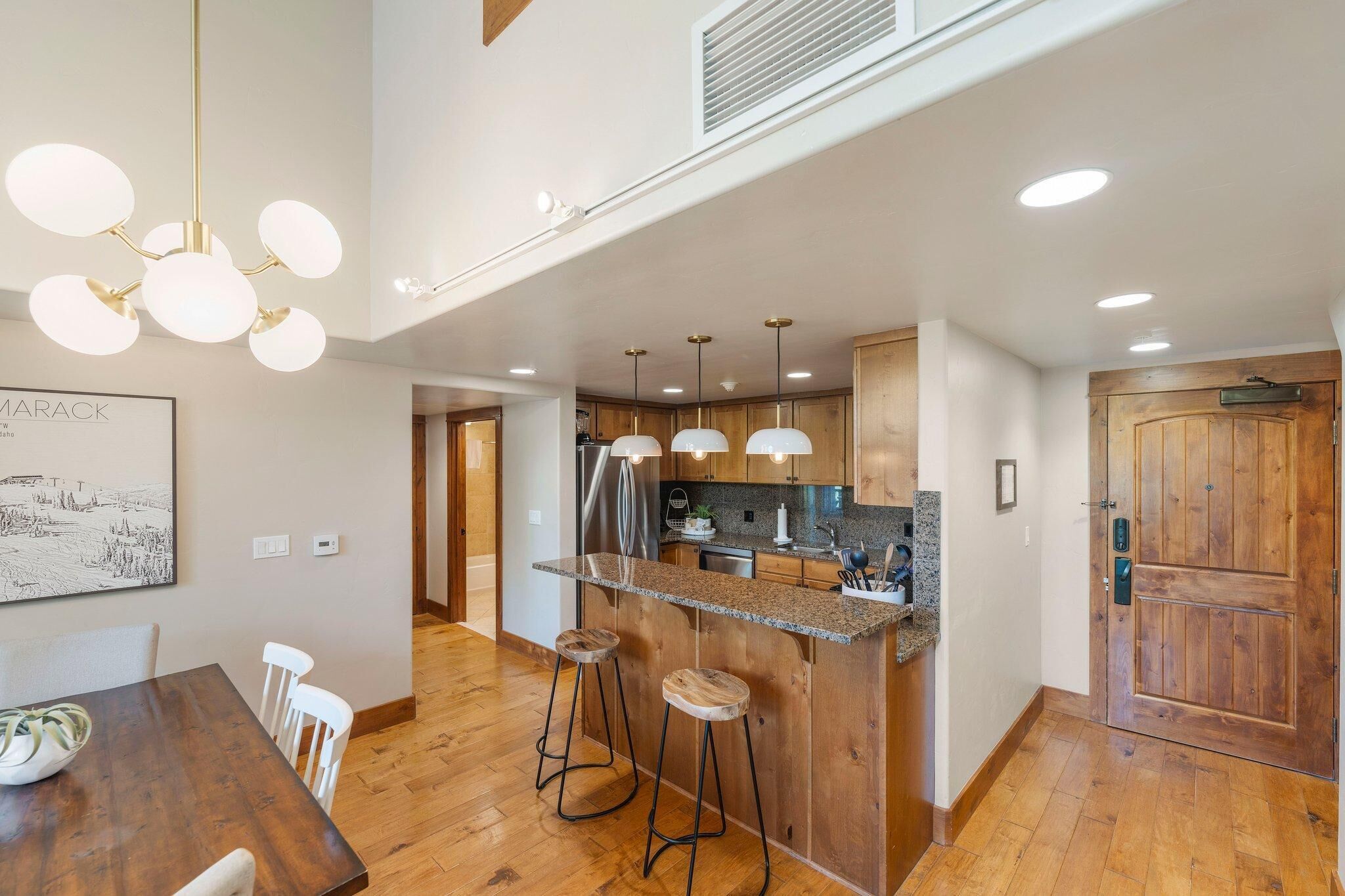 A modern kitchen with a central island, bar stools, pendant lights, and wooden cabinetry.