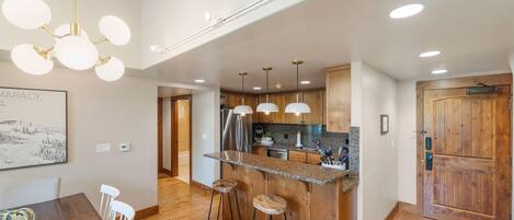 A modern kitchen with a central island, bar stools, pendant lights, and wooden cabinetry.