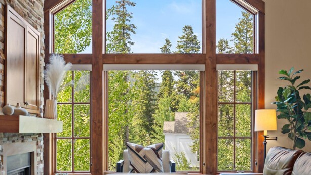 A room with large windows, a fireplace, and a view of trees. - Aspen Grove | Includes Two 1-Day Lift Tickets (Tamarack)