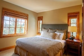 Un dormitorio con una cama grande, cabecera de madera, dos mesitas de noche y una ventana con vista a árboles.