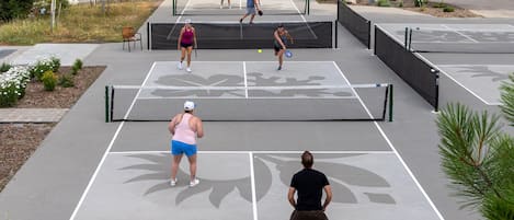 An outdoor tennis court with multiple players, benches, and a surrounding landscaped area.