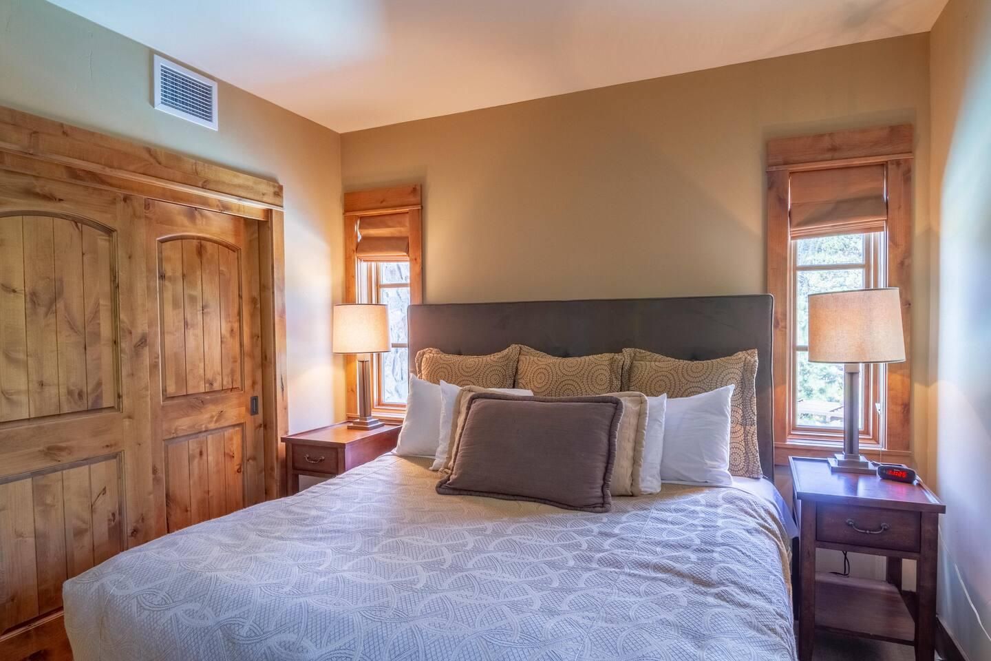 Une chambre à coucher avec un grand lit, une tête de lit en bois, deux tables de chevet avec des lampes et une armoire en bois.