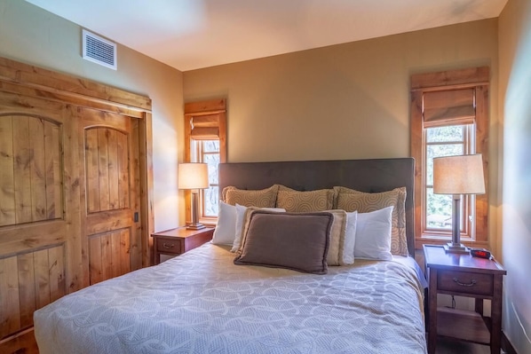 Un dormitorio con una cama grande, cabecera de madera, dos mesitas de noche con lámparas y un armario de madera.