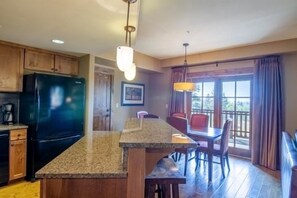 Una cocina con encimeras de granito, armarios de madera, un refrigerador negro y una zona de comedor con mesa y sillas.