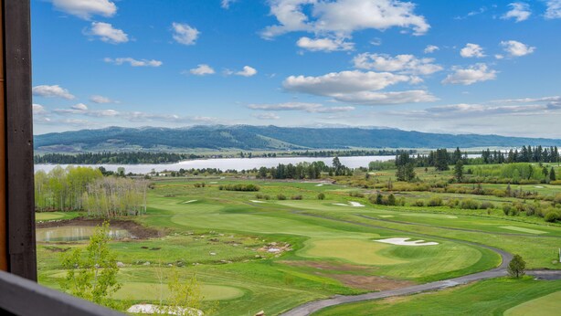 Un campo de golf con un lago y montañas al fondo.