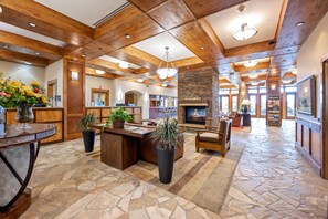 A spacious lobby with a stone floor, wooden ceiling beams, a central fireplace, and a reception desk with potted plants. - Lake View Retreat|Includes Two 1-Day Lift Tickets (Tamarack)