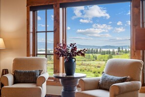 Une pièce avec deux fauteuils placés face à une grande fenêtre donnant sur un paysage verdoyant et des montagnes.