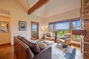 A spacious living room with a leather sofa, two armchairs, a coffee table, and a view of a green landscape through large windows. - Lake View Retreat|Includes Two 1-Day Lift Tickets (Tamarack)