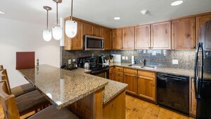 Una cocina con gabinetes de madera, encimeras de granito, refrigerador de acero inoxidable y microondas integrado.