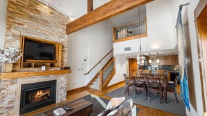 Amplia sala de estar con chimenea de piedra, televisión y comedor con muebles de madera.