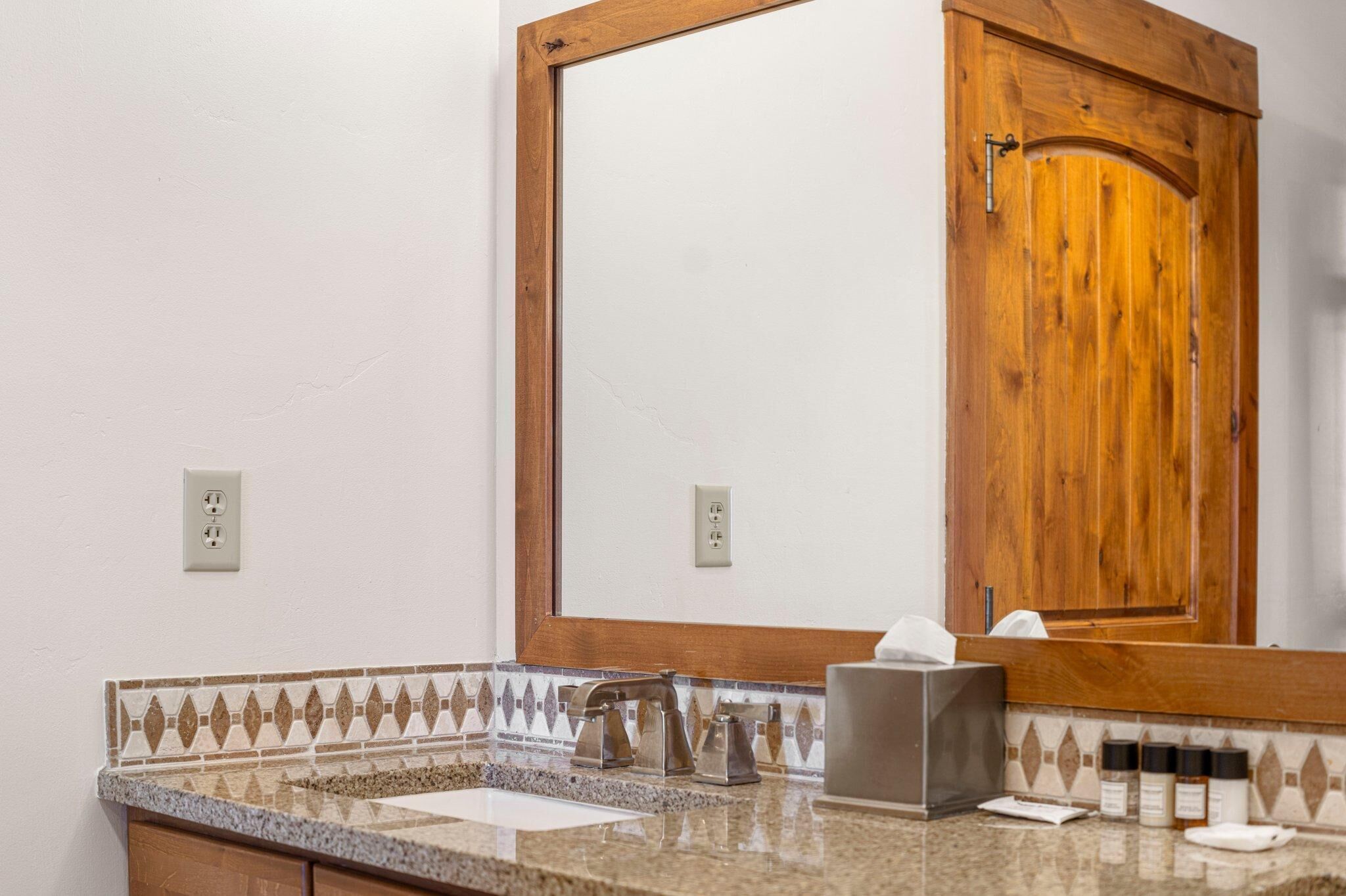 A bathroom with a wooden door, a sink with a mirror, and a towel dispenser.
